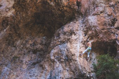 Güçlü bir adam uçuruma tırmanır. Dağcı, doğal bir arazide zorlu bir tırmanış rotasının üstesinden gelir. Türkiye 'de kaya tırmanışı. Güzel turuncu kaya.