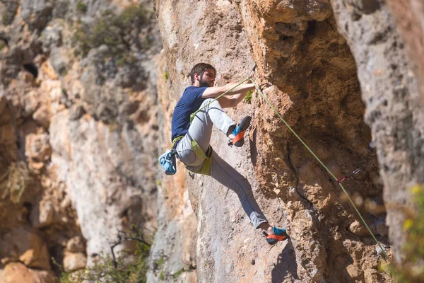 A strong man climbs a cliff. Climber overcomes a difficult climbing route on a natural terrain. Rock climbing in Turkey. Beautiful orange rock.