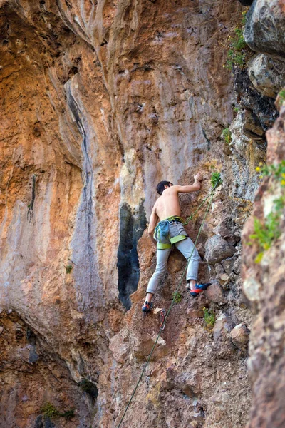 A strong man climbs a cliff. Climber overcomes a difficult climbing route on a natural terrain. Rock climbing in Turkey. Beautiful orange rock.