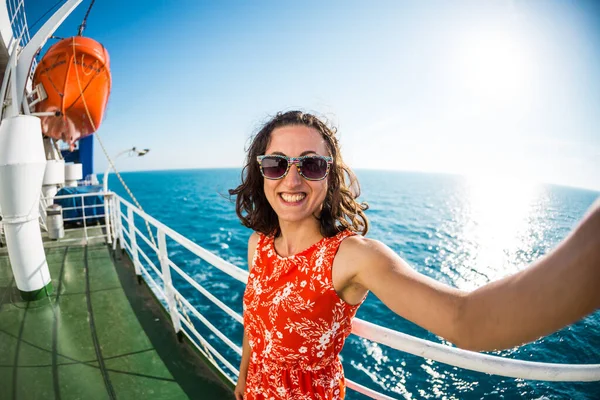 A woman is sailing on a cruise ship, a girl is standing near the fence on a ship against the sea and makes selfie, traveling by ferry, a brunette in a summer dress admires the ocean.