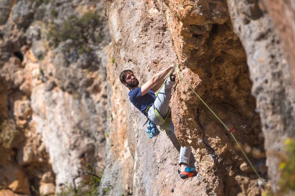 A strong man climbs a cliff. Climber overcomes a difficult climbing route on a natural terrain. Rock climbing in Turkey. Beautiful orange rock.