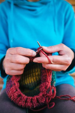 Kadın yün iplikten bir şapka örüyor. Kadın eli, yakın plan. El yapımı. Renkli iplik ve örgü iğneleri.