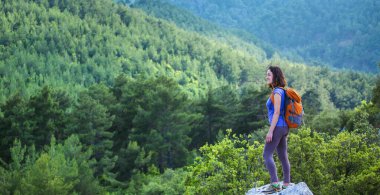 Sırt çantalı bir kadın bir dağın tepesinde durur ve bir dağ vadisinin güzelliğine hayran kalır, güzel yerlere seyahat eder, hedefe ulaşır. Güzel manzara.