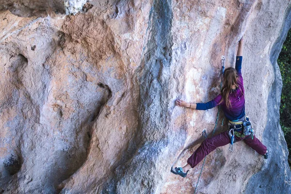 A girl climbs a rock on the background of the forest, The athlete trains in nature, Woman overcomes difficult climbing route, Strong climber, Extreme hobby, Rock climbing in Turkey.