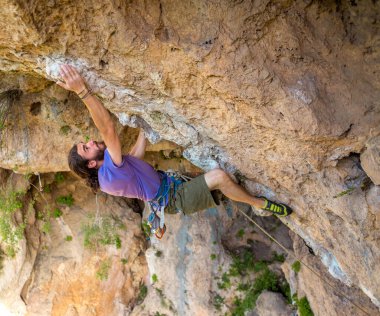 Güçlü bir adam uçuruma tırmanır, dağcı doğal bir arazide zorlu bir tırmanış rotasının üstesinden gelir, Türkiye 'de kaya tırmanışı, güzel turuncu kaya.