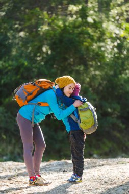 Sırt çantalı bir çocuk annesiyle ormanda yürüyor, çocuk annesine sarılıyor, kadın çocukla seyahat ediyor, annesinin desteği, anneler günü..
