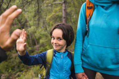 Sırt çantalı bir çocuk ailesiyle birlikte ormanda yürüyor, bir çocuk avucunu uzatıyor, çocuklarla bir gezi, bir çocuk babasına elini uzatıyor..