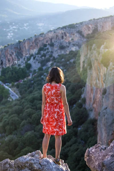 A girl in a red dress on a large rock on top of a mountain against the backdrop of a mountain valley, a trip to the picturesque places of Turkey.