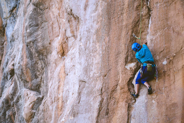 A woman in a helmet climbs a beautiful orange rock. Climbing protective equipment. Safety in climbing. Rock climber overcomes a difficult route on a natural terrain. Rock climbing in Turkey.