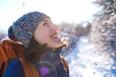 Örgü şapkalı bir kızın portresi. Karlı bir ormanın arka planında sırt çantalı gülümseyen bir kadın. Kış yürüyüşüne çıkmış bir kadın. Kış yükseliyor dağlara.