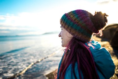 Deniz kıyısında yürürken örgü şapkalı gülümseyen bir kızın portresi, soğuk mevsimde okyanus, Türkiye 'yi gezerken..