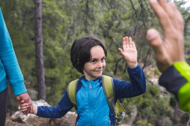 Sırt çantalı bir çocuk ailesiyle birlikte ormanda yürüyor, bir çocuk avucunu uzatıyor, çocuklarla bir gezi, bir çocuk babasına elini uzatıyor..