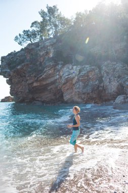 Sahilde yürürken mutlu kaygısız kadın. Deniz kenarında güneşli bir gün. Mutlu yaşam tarzı konsepti. Elbiseli bir kız deniz kıyısında yürüyor..