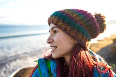 Deniz kıyısında yürürken örgü şapkalı gülümseyen bir kızın portresi, soğuk mevsimde okyanus, Türkiye 'yi gezerken..