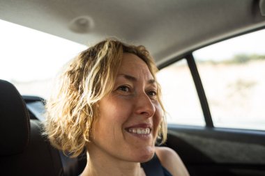 Sarı saçlı, gülümseyen bir kadın arabanın arka koltuğunda oturuyor. Eğlenceli ve güvenli yolculuk.