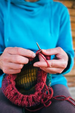 Kadın yün iplikten bir şapka örüyor. Kadın eli, yakın plan. El yapımı. Renkli iplik ve örgü iğneleri.