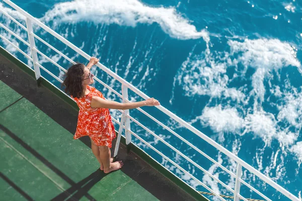 A woman is sailing on a ship, a girl in a summer dress is standing on the deck of a cruise ship, a journey across the ocean, a woman is sailing on a ferry and looks at the water.