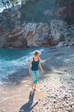 Sahilde yürürken mutlu kaygısız kadın. Deniz kenarında güneşli bir gün. Mutlu yaşam tarzı konsepti. Elbiseli bir kız deniz kıyısında yürüyor..