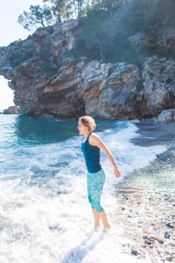 Sahilde yürürken mutlu kaygısız kadın. Deniz kenarında güneşli bir gün. Mutlu yaşam tarzı konsepti. Elbiseli bir kız deniz kıyısında yürüyor..