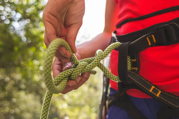 A girl rock climber ties herself with a rope to the harness for safe climbing in the mountains. safety in sports. preparation for rock climbing. doing sports on the street.