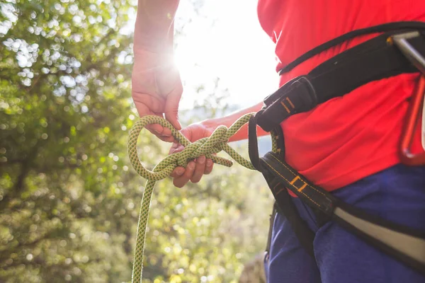 A girl rock climber ties herself with a rope to the harness for safe climbing in the mountains. safety in sports. preparation for rock climbing. doing sports on the street.