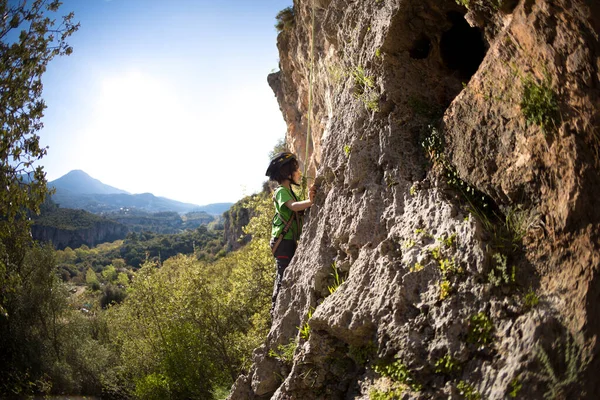 Çocuk doğal bir araziye tırmanıyor. Miğferli bir çocuk dağların arka planında bir kayaya tırmanıyor. Olağanüstü bir hobi. Atletik çocuk güçlü olmayı öğrenir. Kaya tırmanışı güvenli.
