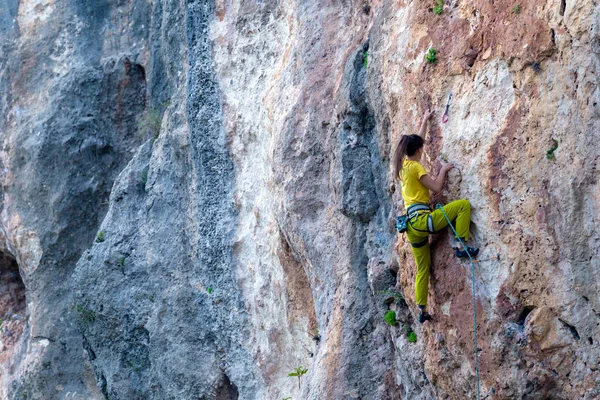 A girl climbs a rock on the background of the forest, The athlete trains in nature, Woman overcomes difficult climbing route, Strong climber, Extreme hobby, Rock climbing in Turkey.