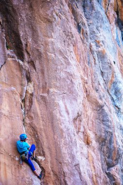Kasklı bir kadın güzel mavi bir kayaya tırmanır. Koruyucu ekipmana tırmanıyorum. Tırmanırken güvenlik. Kaya tırmanışçısı doğal bir arazide zorlu bir rotanın üstesinden gelir. Türkiye 'de kaya tırmanışı.