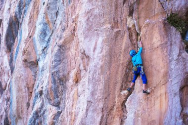 Kasklı bir kadın güzel mavi bir kayaya tırmanır. Koruyucu ekipmana tırmanıyorum. Tırmanırken güvenlik. Kaya tırmanışçısı doğal bir arazide zorlu bir rotanın üstesinden gelir. Türkiye 'de kaya tırmanışı.