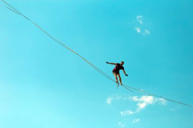 Mavi gökyüzünün arka planındaki Highliner bir hamle yapıyor. Bir adam askı manzarası boyunca aşağıdan yürüyor. Performans ip cambazı. İnsanoğlu uçurumun üzerinde denge kurar. İleriye doğru kararlı bir adım.
