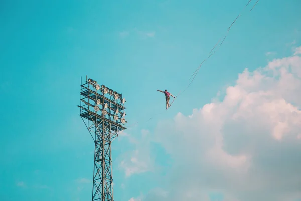 高耸在蓝天的背景上 一个男人沿着一条在塔与塔之间伸展的吊带走着 走钢丝的表演 一个人正在悬崖峭壁上保持平衡 向前迈出决定性的一步 — 图库照片