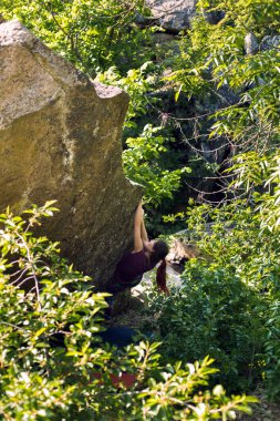 Kız kaya tırmanışçısı bir taşa tırmanır. Doğada kayalaşma