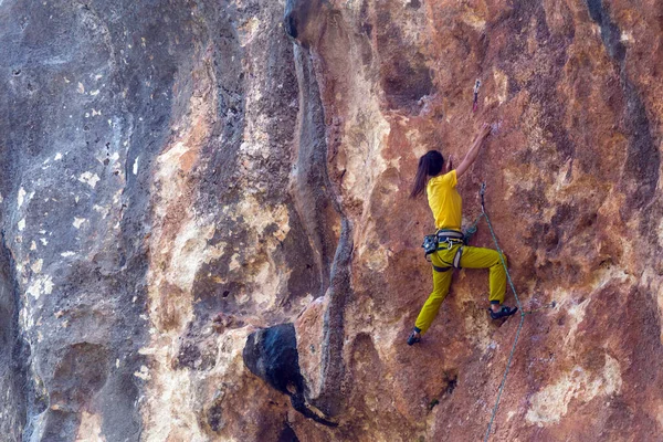 A girl climbs a rock on the background of the forest, The athlete trains in nature, Woman overcomes difficult climbing route, Strong climber, Extreme hobby, Rock climbing in Turkey.