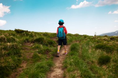 Bir çocukla dağlarda yürümek, sırt çantalı bir çocuk dağ yolunda yürümek, çocuklar için açık hava eğlencesi..