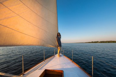 bir yatla seyahat etmek. Kız geminin pruvasında duruyor ve uzaklığa bakıyor. Beyaz bir yatın güvertesinde dinleniyor..