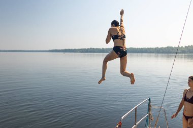 Gün batımında bir kız yelkenli yatından suya atlıyor. Suyun üzerinde dinlenin. Eğlence zamanı. tatil macerası
