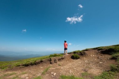 Bir çocuk dağın tepesinde durur ve uzaklığa bakar, bir çocuk yürüyüşe çıkar, çocuklarla bir geziye çıkar, bir çocuk tepeye tırmanır.