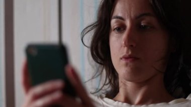 Gülümseyen kız kanepede uzanıyor ve akıllı telefona bir mesaj yazıyor, kadın dinleniyor, esmer kız okuyor ve gülümsüyor.