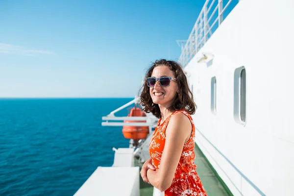 A woman is sailing on a cruise ship, a girl is standing near the fence on a ship and looking at the sea, traveling by ferry, a brunette in a summer dress admires the ocean.