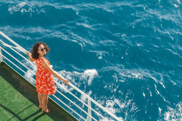 A woman is sailing on a ship, a girl in a summer dress is standing on the deck of a cruise ship, a journey across the ocean, a woman is sailing on a ferry and looks at the water.