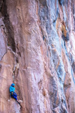Kasklı bir kadın güzel mavi bir kayaya tırmanır. Koruyucu ekipmana tırmanıyorum. Tırmanırken güvenlik. Kaya tırmanışçısı doğal bir arazide zorlu bir rotanın üstesinden gelir. Türkiye 'de kaya tırmanışı.