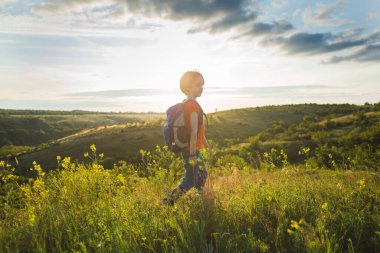Yürüyüşe çıkmış sırt çantalı bir çocuk. Bir çocukla yürüyüşe çıkmak. Doğada yaz tatili.