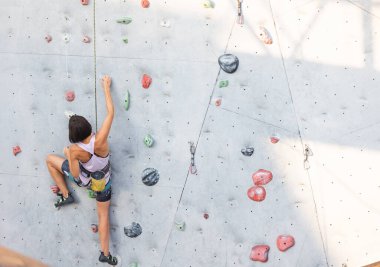 Kız tırmanma duvarına tırmanıyor. Kaya tırmanışı şehirde etkin bir eğlence türüdür. Doğada spor yapmak