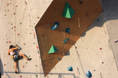 Kız tırmanma duvarına tırmanıyor. Kaya tırmanışı şehirde etkin bir eğlence türüdür. Doğada spor yapmak