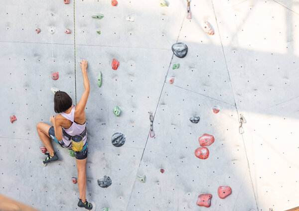 девушка лезет на стену для скалолазания. скалолазание как вид активного отдыха в городе. спорт на природе
