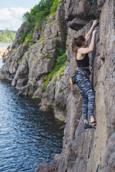 一个女孩爬上水面上的岩石 一个女人从事极端的运动 在自然的地形上攀岩 力量和耐力训练 — 图库照片