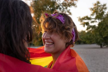 Genç lezbiyen çift şefkatle sarılıyor. Sokakta gökkuşağı bayrağı. Igbt topluluğu için eşit haklar, samimiyet ve iki kız için hisler