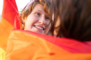 Genç lezbiyen çift şefkatle sarılıyor. Sokakta gökkuşağı bayrağı. Igbt topluluğu için eşit haklar, samimiyet ve iki kız için hisler