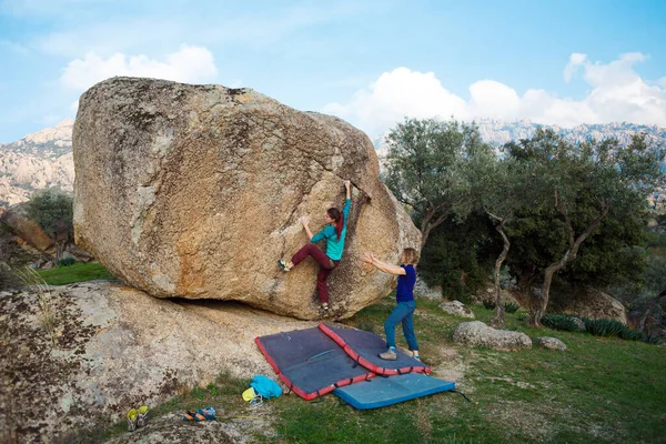 Friends go in for sports in nature, bouldering on rocks, girl climbs a big stone, woman is belayng partner, outdoor recreation, bouldering on the