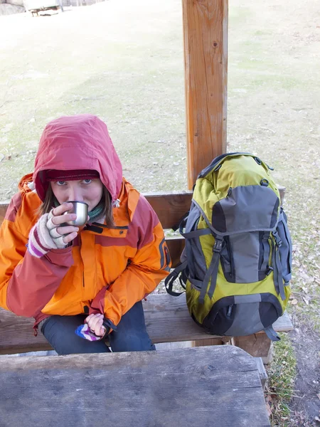 Das Mädchen sitzt an einem Tisch und trinkt aus einer Thermoskanne. — Stockfoto